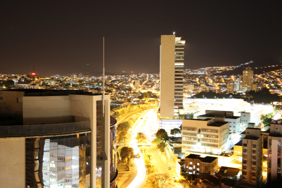 Fotografia noturna, vista panorâmica da cidade. Rio Arrudas ao centro, prédios iluminados.