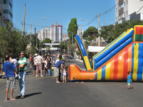 Crianças em brinquedo inflável gigante na via, ao lado de adultos que conversam livrmente