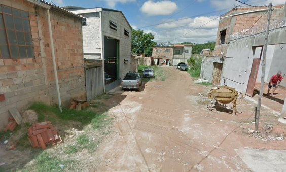 Rua sem asfalto com casas à direita e à esquerda, durante o dia. 