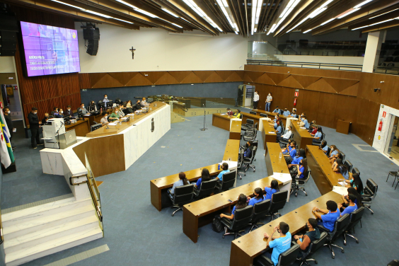 Plenário visto do alto. É possível ver a mesa com os vereadores e as cadeiras ocupadas por adolescentes que participaram da audiência