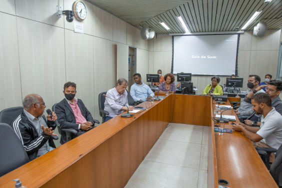 Duas mulheres e sete homens sentados à mesa em reunião.