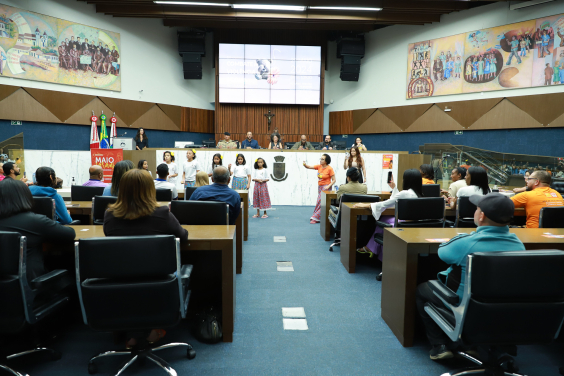 Acompanhada por adulta, cinco crianças de saia de chita e flor no cabelo se apresentam no Plenário Amintas de Barros.