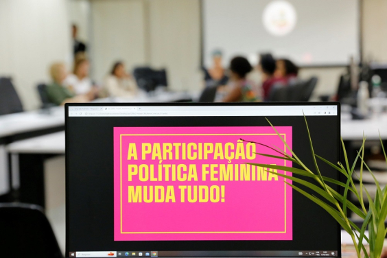 Reunião com mulheres com cartaz em primeiro plano: A participação política feminina muda tudo!