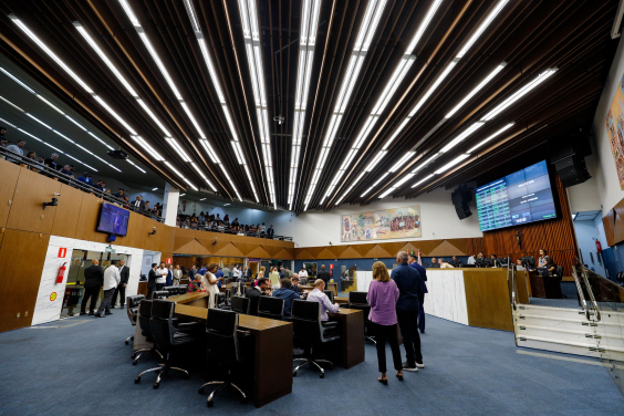 Vereadores se reúnem presencialmente na primeira reunião do Plenário da 20ª Legislatura. A foto mostra vereadores sentados e em pé, em visão lateral, bem como a mesa diretora e o telão.