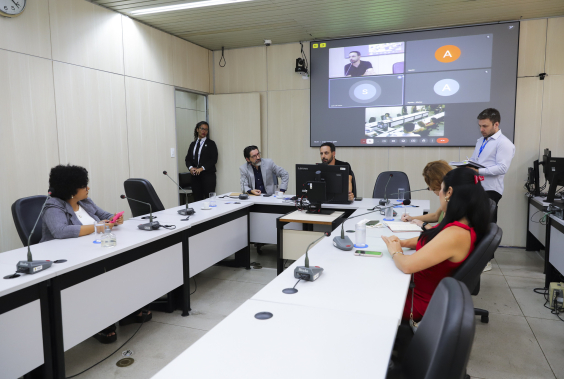 Vereadores no Plenário Helvécio Arantes, sentados com microfones na mesa à frente deles, e um telão atrás.