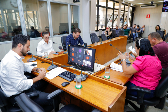 Vereadores discutem projetos no Plenário Camil Caram. A tela do computador à frente do presidente Uner Augusto mostra videochamada com vereadores presentes virtualmente.