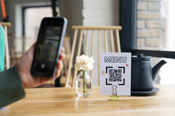 Mão com celular fazendo leitura de QR code em cima de uma mesa