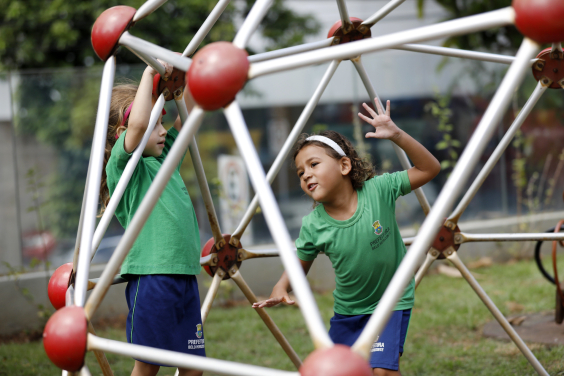 Crianças brincam em parquinho da Emei Timbiras usando uniformes escolares com blusa verde e short azul