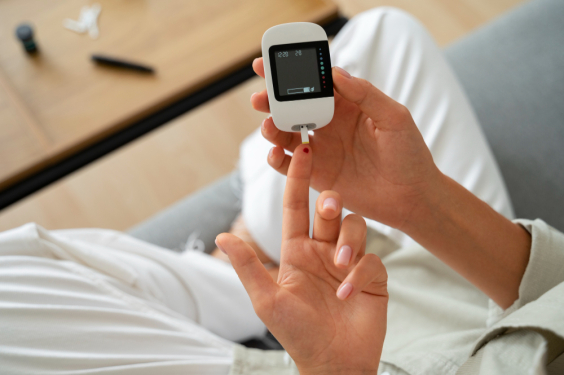 Vista superior de mulher com diabetes verificando seu nível de glicose em um aparelho medidor; ela tem o dedo furado com uma gota de sangue