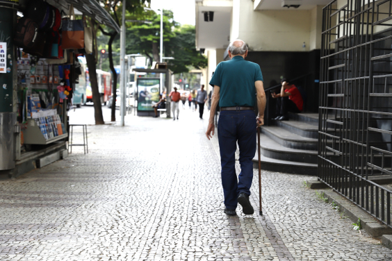 Idoso visto de costas caminha em rua de BH com bengala