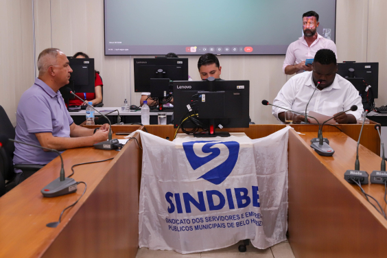 Vereadores em reunião no Plenário Camil Caram; bandeira do Sindibel está erguida na frente da mesa do presidente da comissão