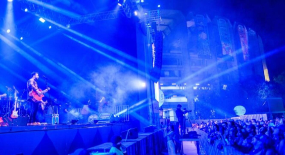 imagem de show musical em ambiente escuro, luzes neon, com vista do palco e da plateia