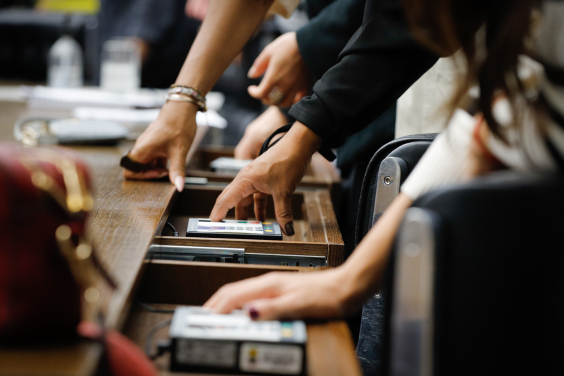 mãos de parlamentares operando terminal de votação