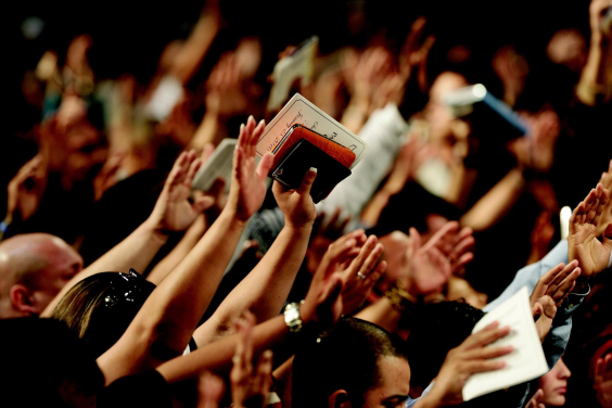 pessoas com o braço levantado em culto religioso