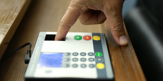 Mão fazendo leitura biométrica de digital em equipamento de votação