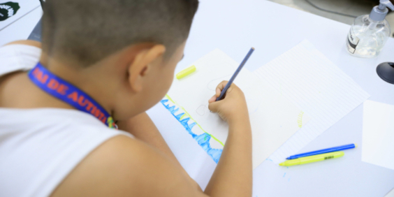 Criança vista de costas escrevendo em caderno com lápis