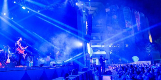 imagem de show musical em ambiente escuro, luzes neon, com vista do palco e da plateia
