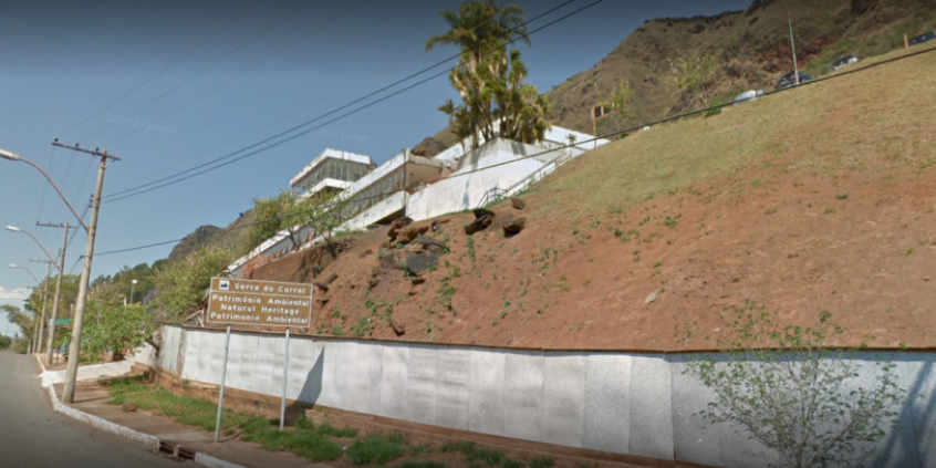 vista panorâmica da fachada do antigo hospital Hilton Rocha e parte da Serra do Curral. Placa sinaliza a área como patrimônio ambiental