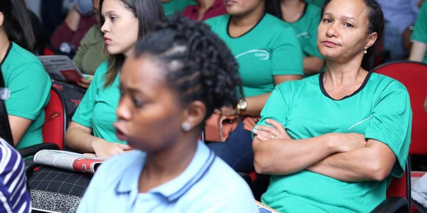 Trabalhadores das escolas ocupam as cadeiras do plenário. Mulher cruza os braços em sinal de reprovação