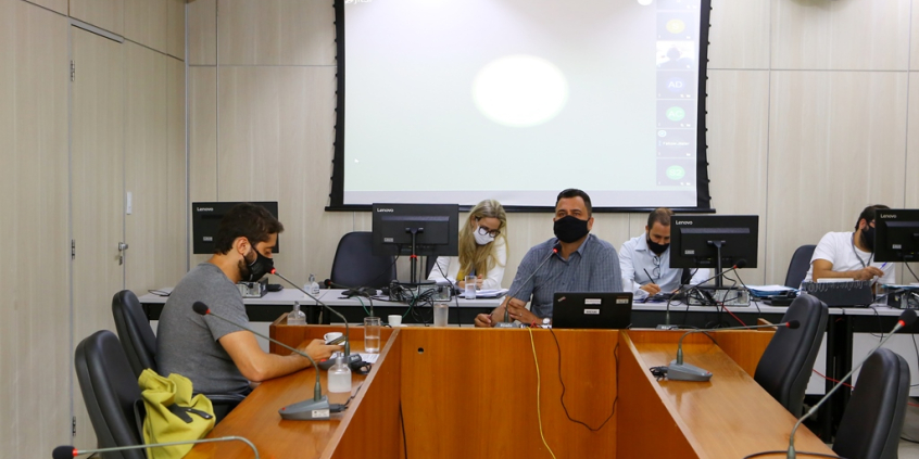 Vereadores compõem mesa de reunião no plenário Camil Caram. No telão, ao fundo, outros vereadores em videoconferência
