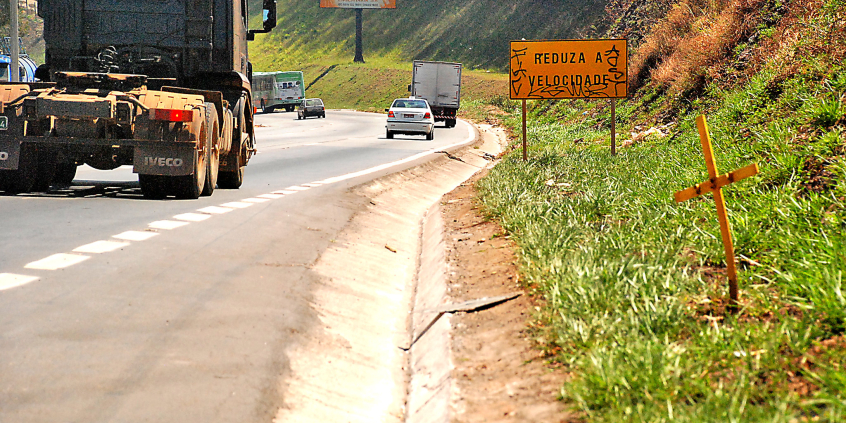 trecho de rodovia, com caminhão trafegando, sem acostamento ou áreas de escape. Placa indica redução de velocidade