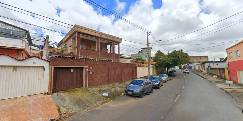 Foto de rua residencial, com mão dupla, casas e cinco carros estacionados à esquerda, durante o dia