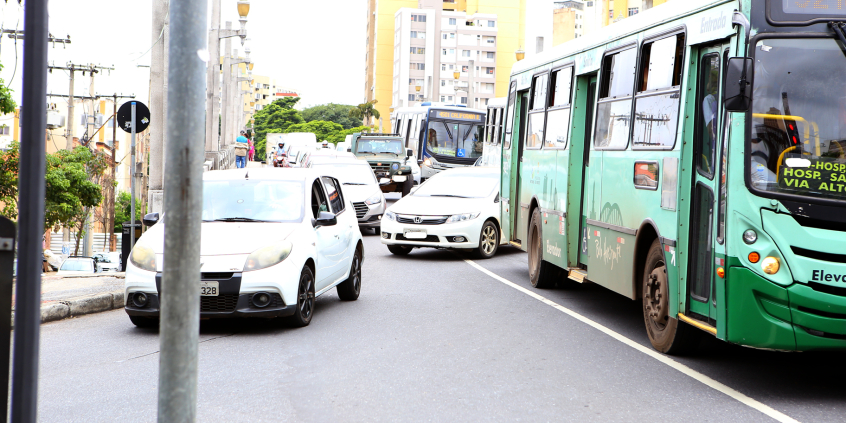 Dois ônibus e três carros à frente de um trânsito cheio de veículos.