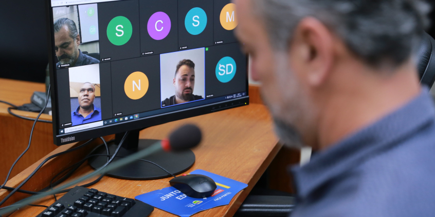 Vereador olha tela de computador que exibe reunião remota com a imagem de dois outros vereadores.