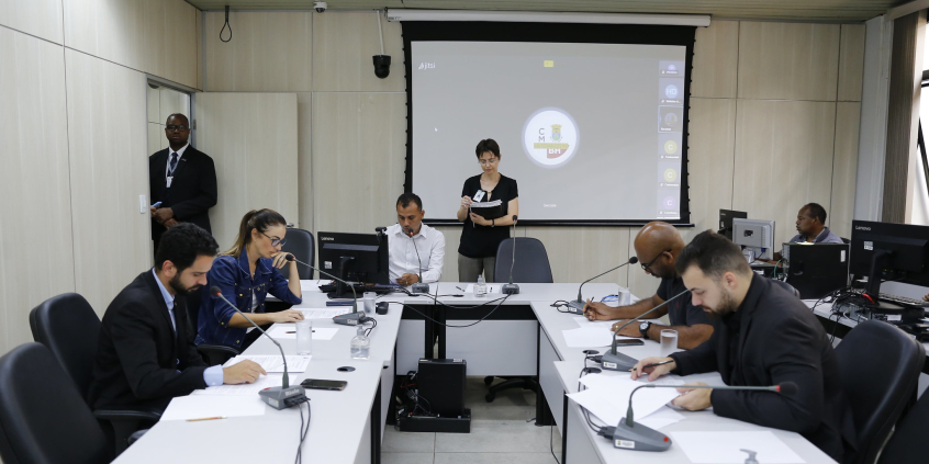 cinco vereadores reunidos, sentados à mesa, acompanhados de três assessores ao fundo. 