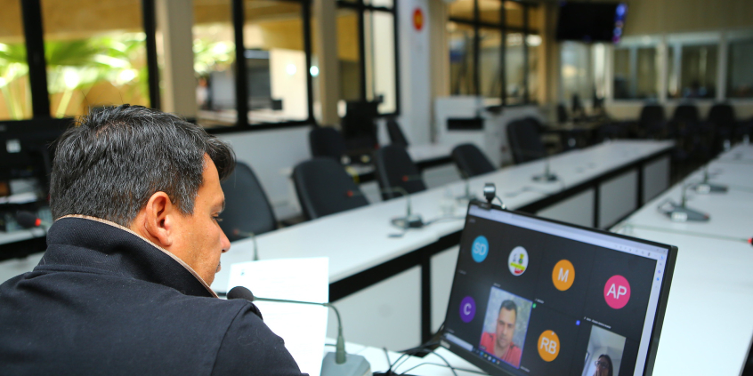 Vereador, sentado em frente ao computador, participa de reunião virtual e olha para tela com a imagem de dois outros parlamentares.