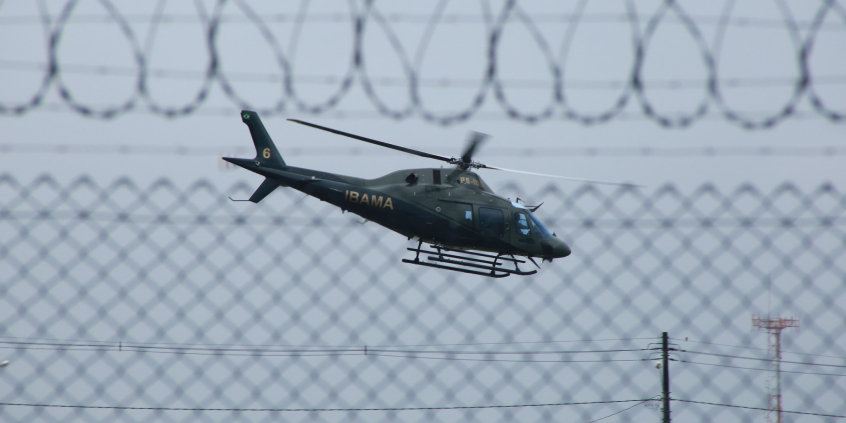 Imagem de um helicóptero no ar. é possível ver a cerca de segurança no local 
