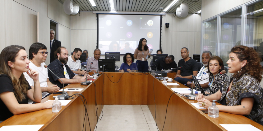 Quatro mulheres e sete homens em reunião, sentados à mesa.