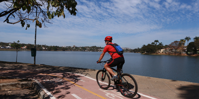 Homem anda de bicicleta em ciclovia da orla da Lagoa da Pampulha, durante o dia. 