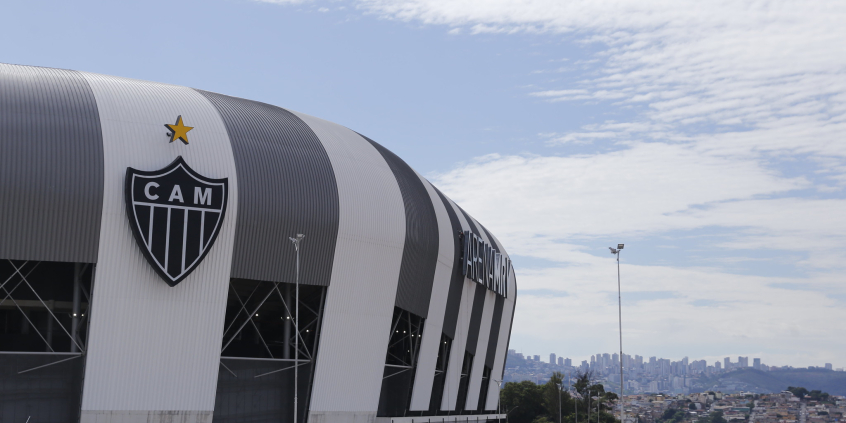 Foto da Fachada da Arena MRV, com a cidade ao fundo, durante o dia.