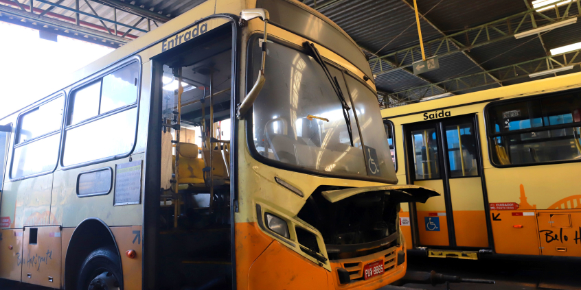 Imagem de dois ônibus amarelos com portas abertas e motor à mostra, indicando que estão em manutenção