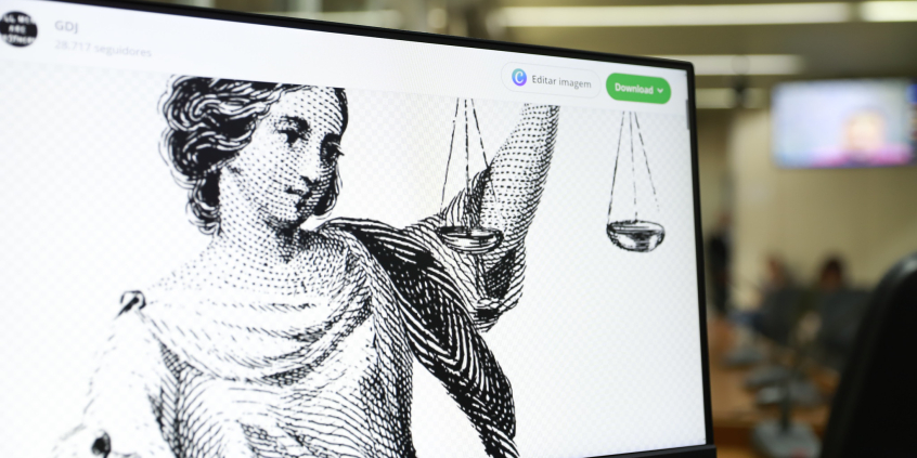 Imagem de mulher em Preto e Branco segurando uma balança, simbolizando a Justiça, é exibida na tela de um computador 
