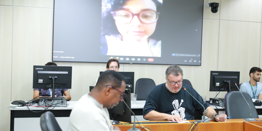 Imagem dos vereadores Pedro Patrus e Gilson Guimarães durante a reunião. A vereadora Iza Lourença aparece na imagemdo telão ao fundo