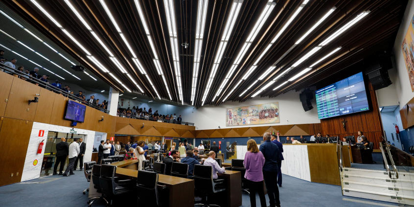 Vereadores se reúnem presencialmente na primeira reunião do Plenário da 20ª Legislatura. A foto mostra vereadores sentados e em pé, em visão lateral, bem como a mesa diretora e o telão.