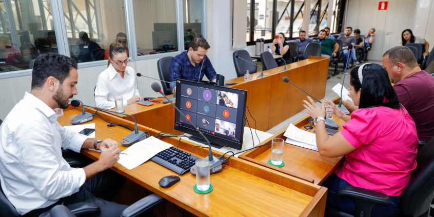 Vereadores discutem projetos no Plenário Camil Caram. A tela do computador à frente do presidente Uner Augusto mostra videochamada com vereadores presentes virtualmente.