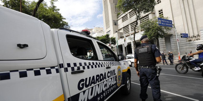 agente da guarda municipal de Belo Horizonte visto de costas ao lado de veículo da corporação