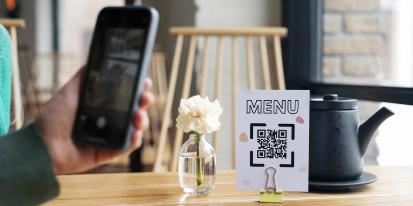 Mão com celular fazendo leitura de QR code em cima de uma mesa