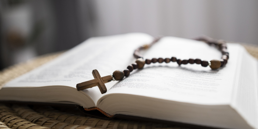 imagem de uma bíblia aberta ao meio e um terço disposto sobre as páginas