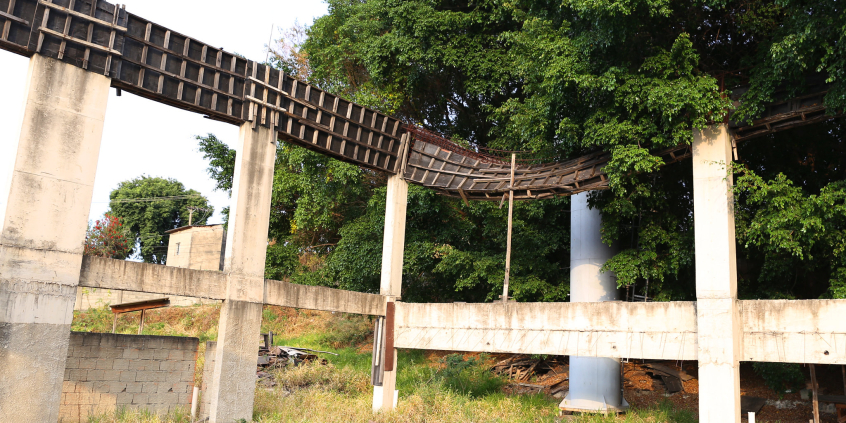 Pilares de obra abandonada em meio a terreno com mato alto