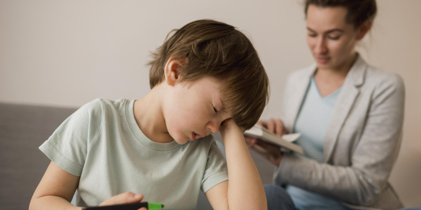 Criança demonstra cansaço enquanto mãe ensina em casa