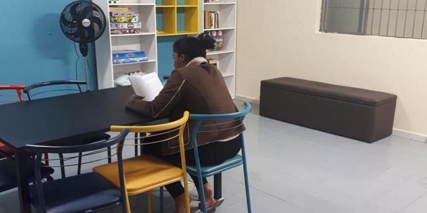 interior de unidade de acolhimento temporário com adolescente sentada de costas em uma mesa