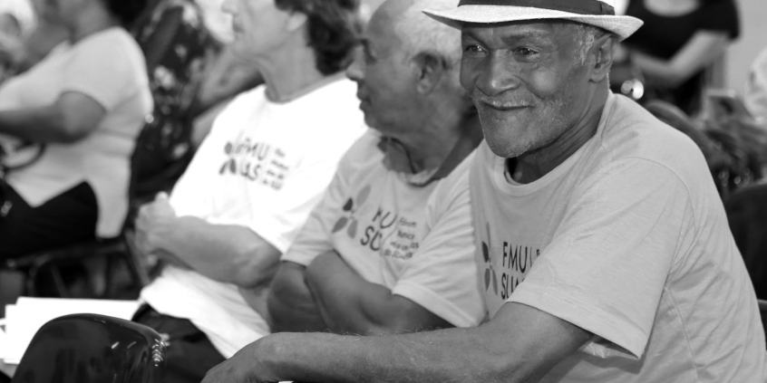 Imagem em preto e branco de três homens idosos sentados lado a lado 