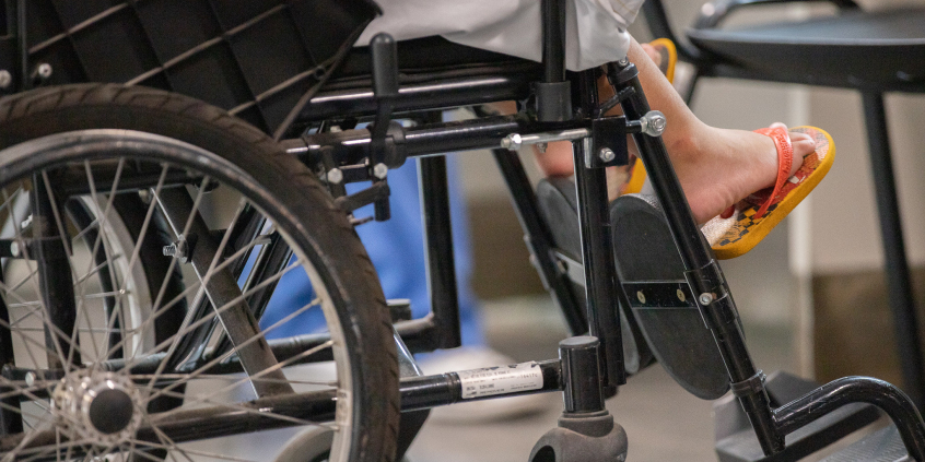 Pessoa com chinelo laranja sentada em cadeira de rodas