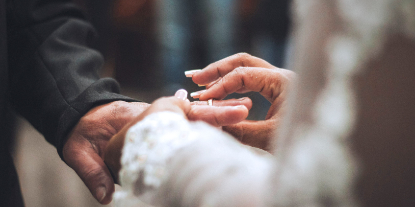 Imagem fechada nas mãos de um casal trocando alianças 