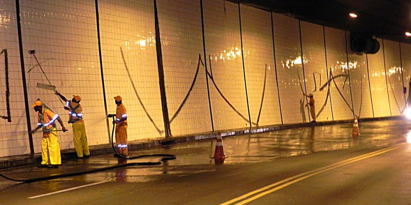 funcionários de limpeza pública fazem remoção de pichação em paredes de túnel