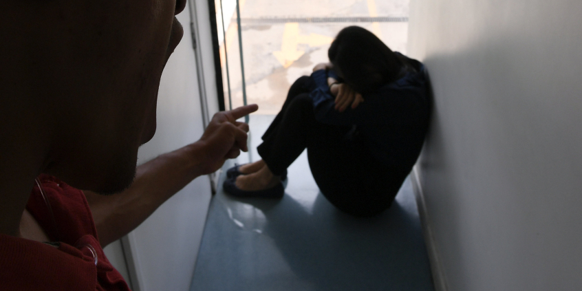 homem de pé aponta para mulher sentada no chão em cena de violência